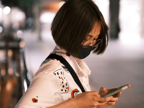 A photograph of a person wearing a N95 mask texting on their phone. 