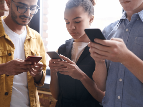 A photograph of 3 people standing close together looking at their phones