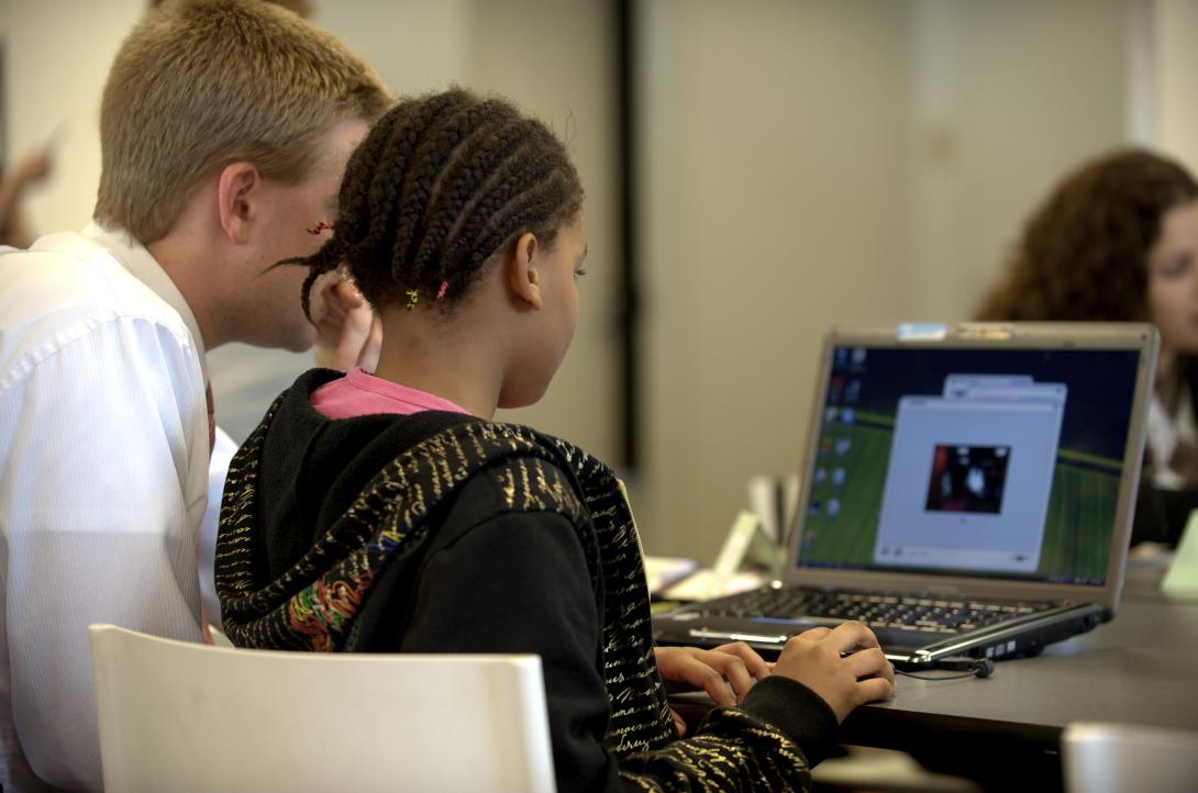 A photograph of a child typing on a computer next to a teacher