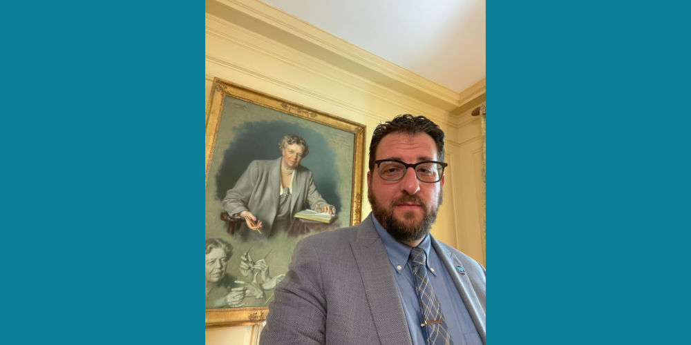 A photograph of Free Press Co-CEO Craig Aaron at the White House with a painted portrait of Eleanor Roosevelt behind him